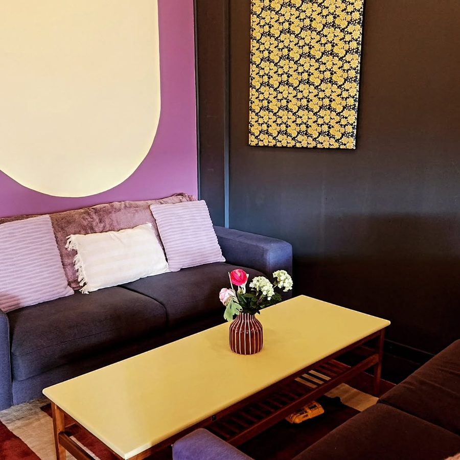 Lounge corner with a purple wall, navy sofa and a yellow coffee table with flowers