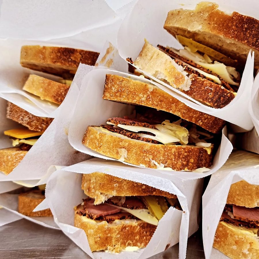 A stack of toasties in paper wraps, filled with pastrami, Swiss cheese and sauerkraut